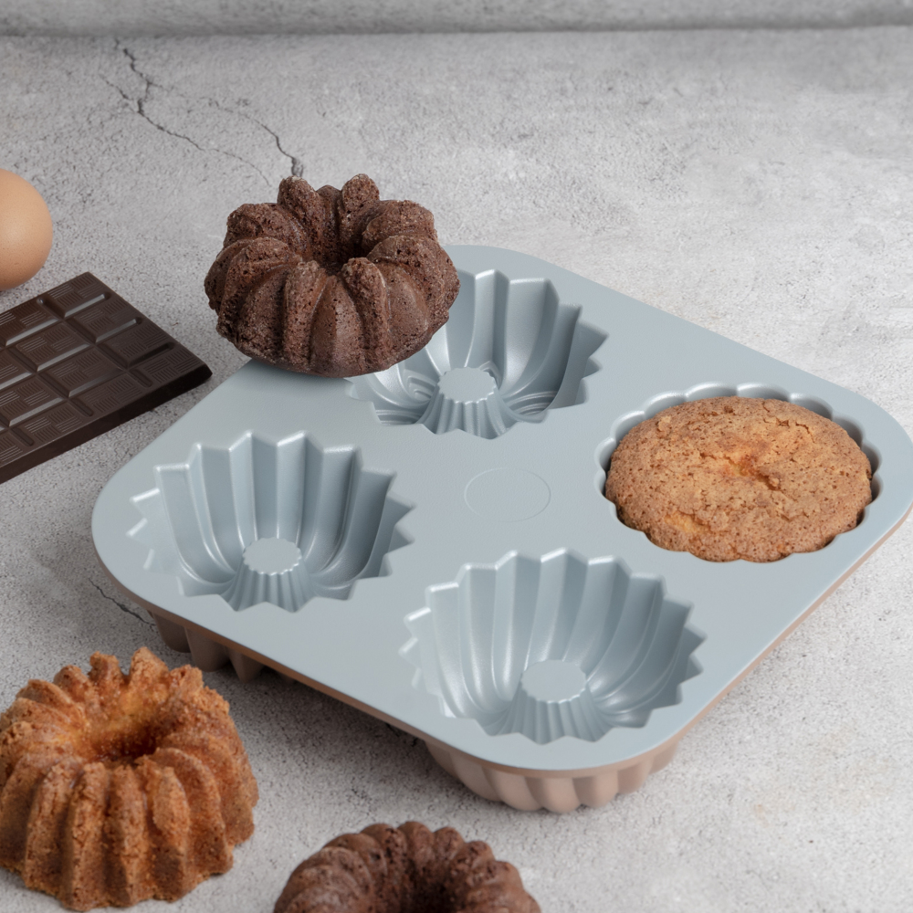 A six-piece silicone mold for making mini bundt cakes and cupcakes, shown with several baked brown pastries on a light gray textured surface.