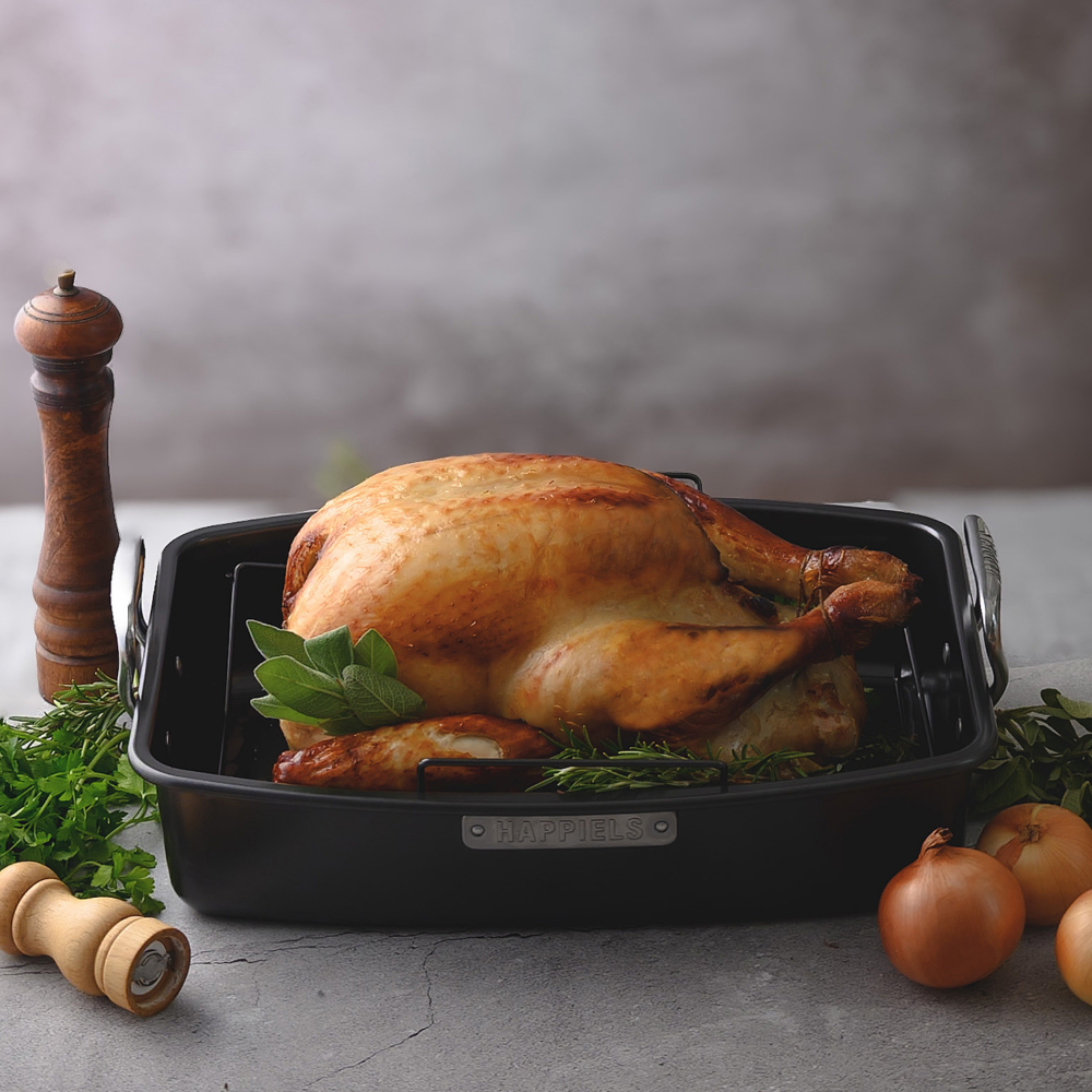 Roasted chicken in a roasting pan on a gray surface with herbs and onions.